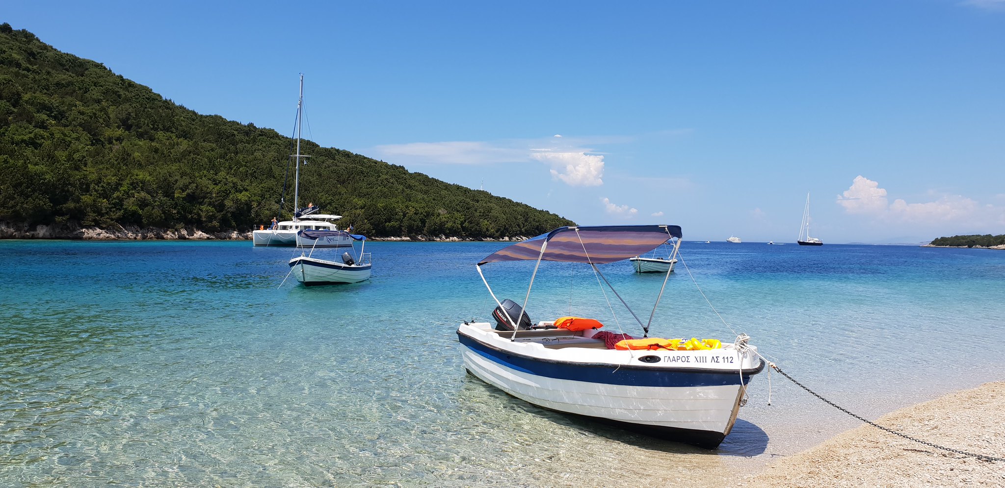 Βάρκες και ένα καταμαράν στα καταγάλανα νερά σε παραλία στα Σύβοτα