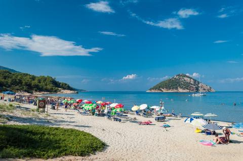 Ομπλέλες και λουόμενοι στην παραλία παράδεισος της Θάσου και στο φόντο η θάλασσα και το νησάκι Κοινήρα