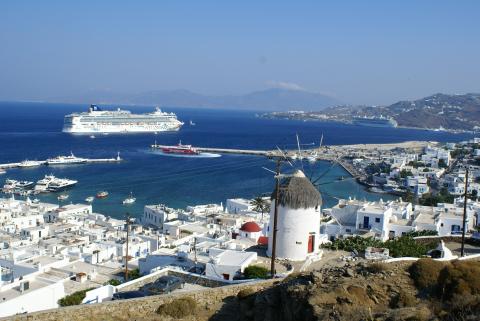 Ένας ανεμόμυλος με την πανοραμικής άποψη της πόλης της Μυκόνου και ένα κρουαζιερόπλοιο νε προσεγγίζει το νέο λιμάνι του νησιού μυκονοσ αξιοθεατα